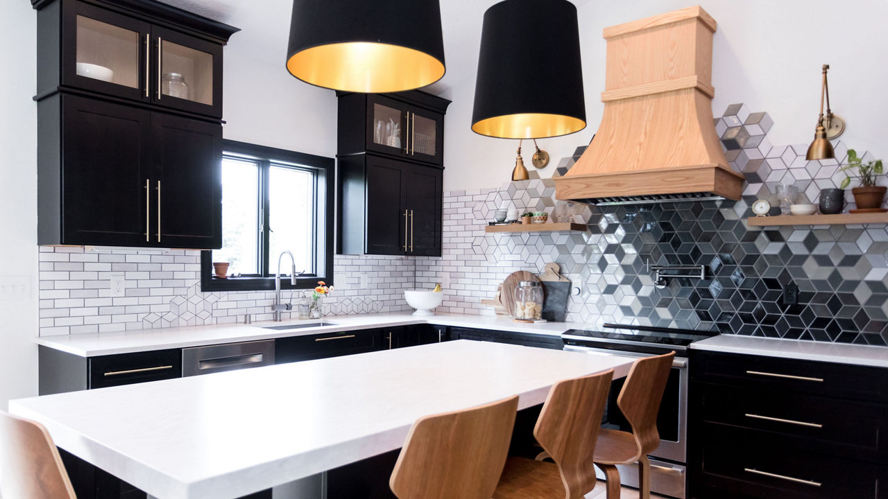 a black and white kitchen with black cabinets topped with white quartz countertops, a center island with 4 wooden barstools, a wooden hood over the range, and a black and white ombre hexagonal backsplash