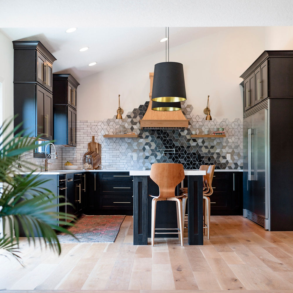 A kitchen with black cabinets, a unique tiled backsplash, wooden shelving, hood, and bar stools, and white quartz countertops.