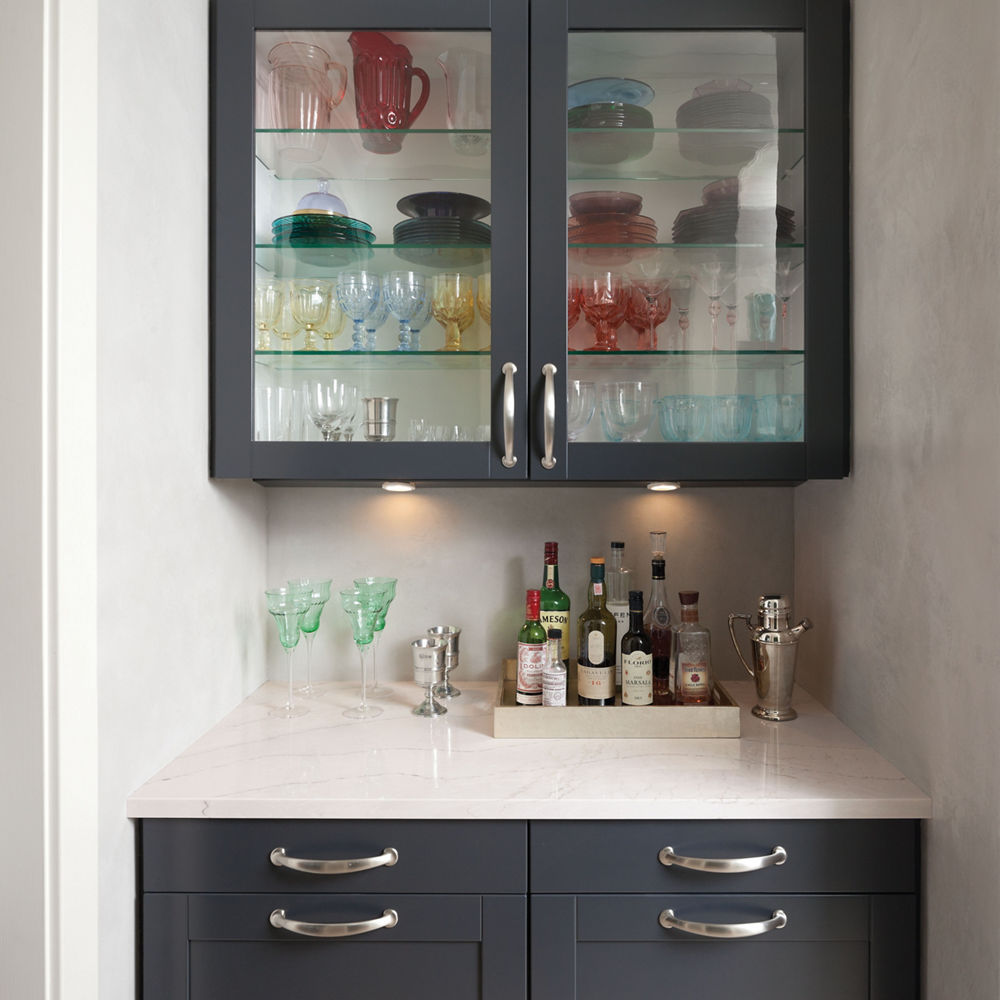 A dry bar white matte black cabinets, white quartz countertops, and upper cabinetry with glass windows.