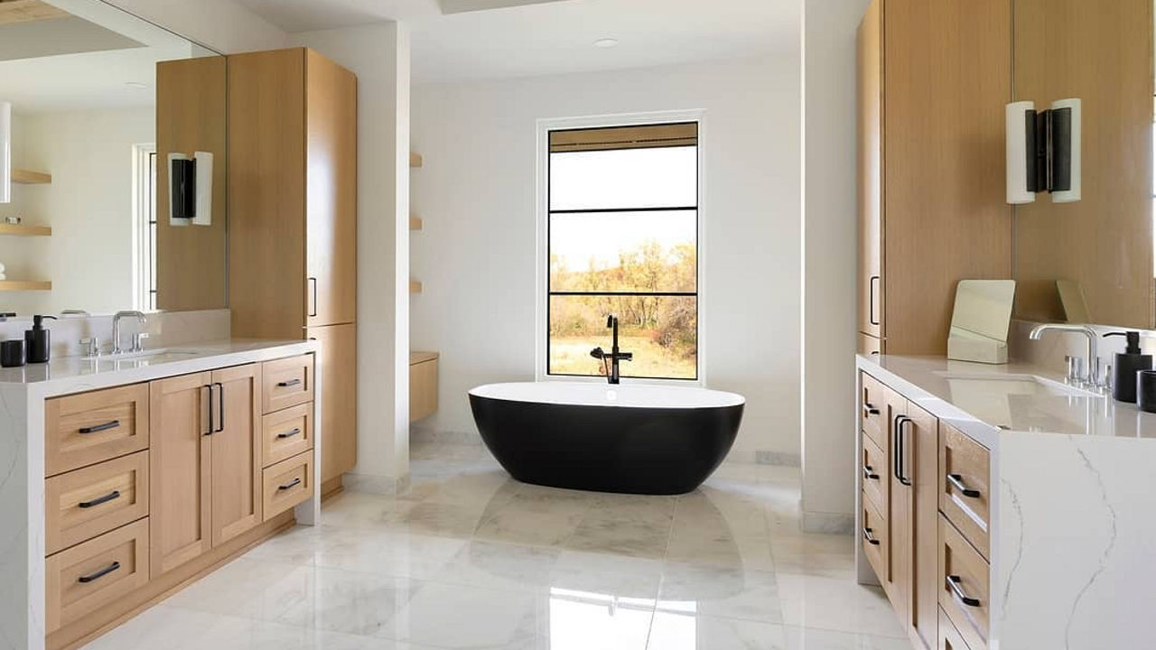 A white kitchen with two waterfall vanities are separated by a black bathtub.