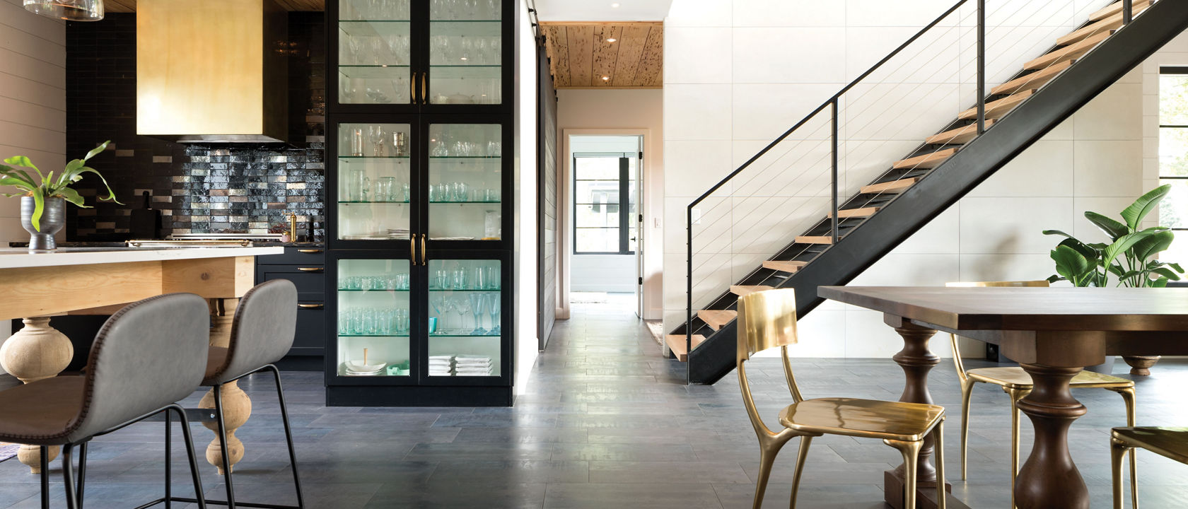 a kitchen and dining room with dark wooden floors, black cabinets, wooden accents, and gold chairs. 