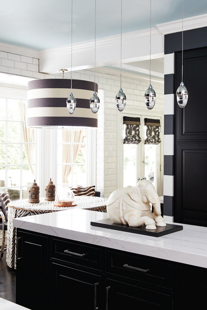 a bold black and white kitchen with black cabinets, white quartz countertops on the island, 6 pendant lights, one striped chandelier above the dining table