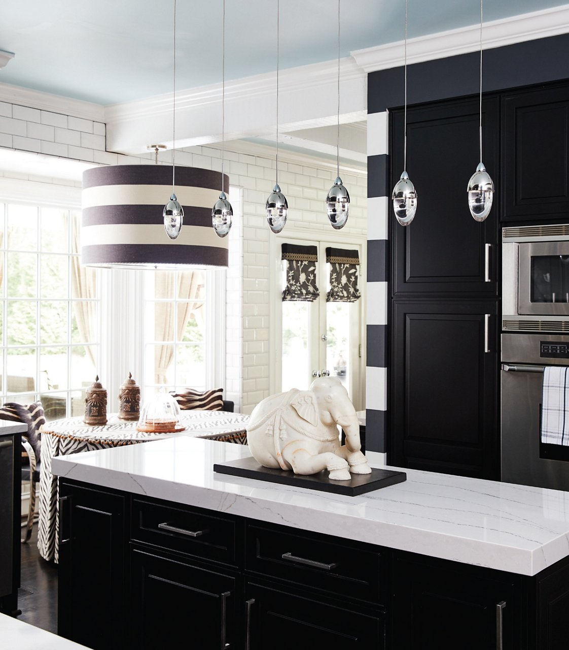 a bold black and white kitchen with black cabinets, white quartz countertops on the island, 6 pendant lights, one striped chandelier above the dining table