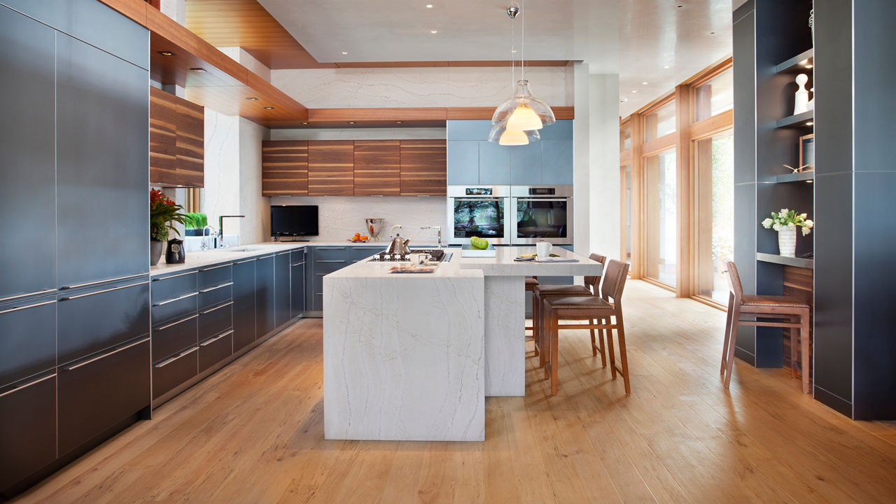 a modern kitchen with sleek black cabinets, wooden upper cabinets, a center double waterfall-edge island topped with white quartz countertops with two pendant lights overhead