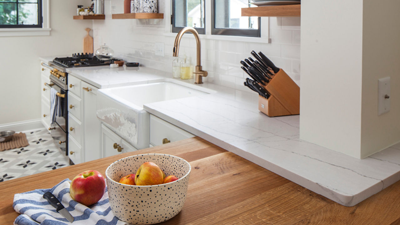 A kitchen with an island made from butcher block countertops with an overlay of white quartz countertops that creates a modern look in a more traditional kitchen