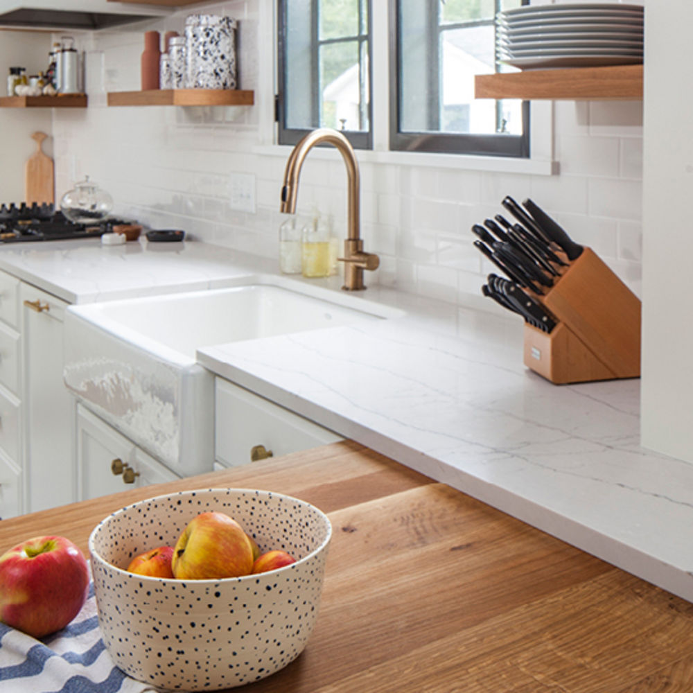 A kitchen with an island made from butcher block countertops with an overlay of white quartz countertops that creates a modern look in a more traditional kitchen