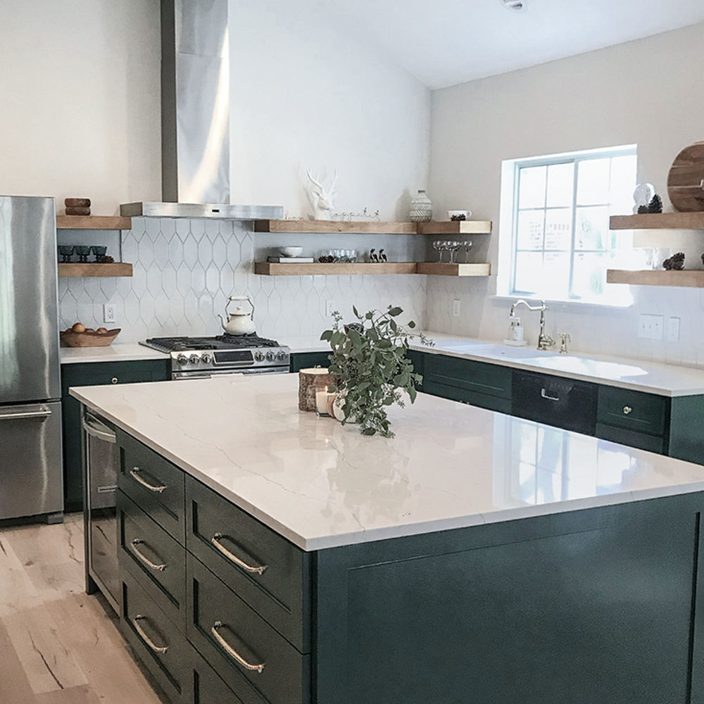 a kitchen with emerald green lower cabinets, wooden open shelving, white quartz countertops, white tile backsplash, and stainless steel appliances.