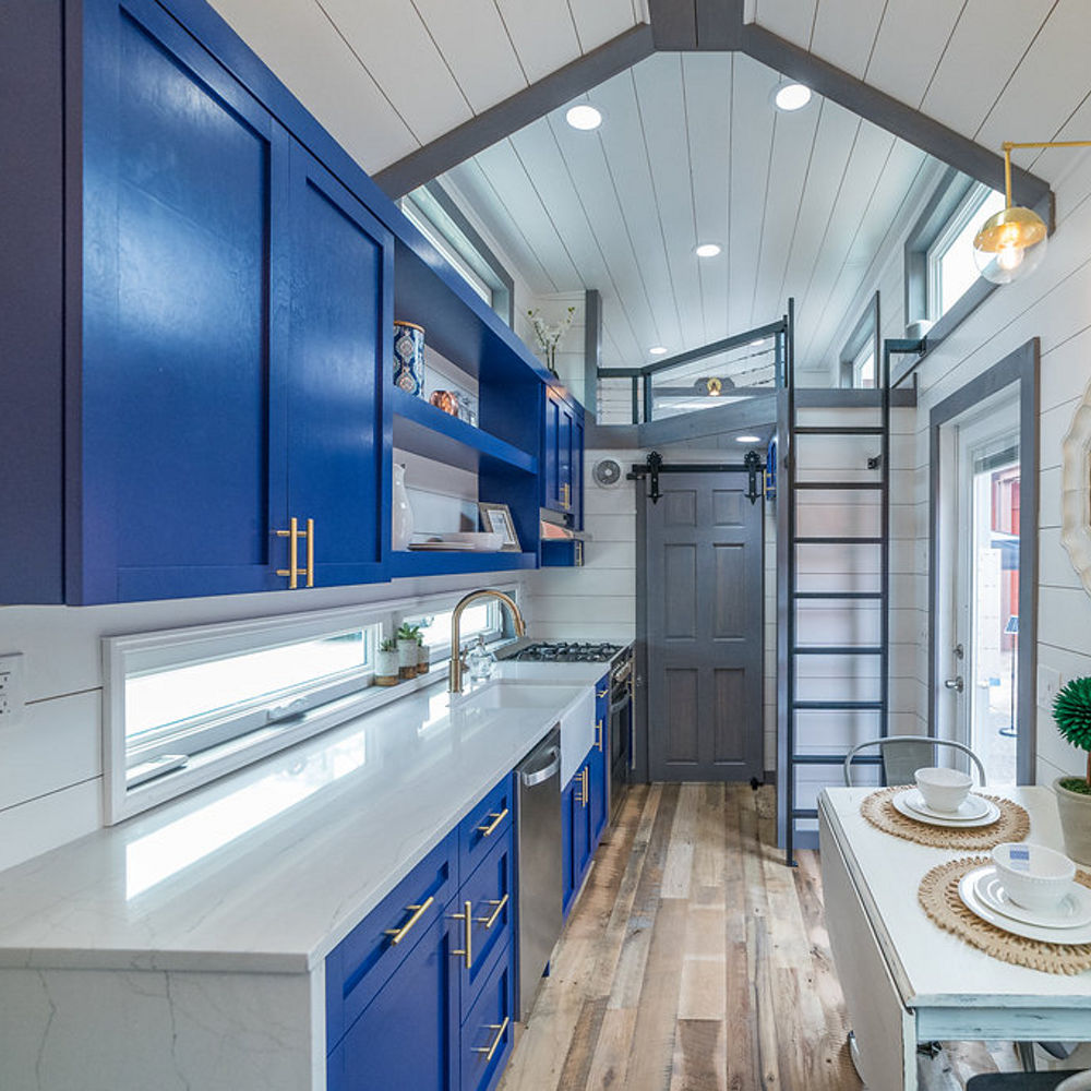 Tiny home kitchen with cobalt blue cabinets, Cambria Ella countertops, and white shiplap ceiling and walls.