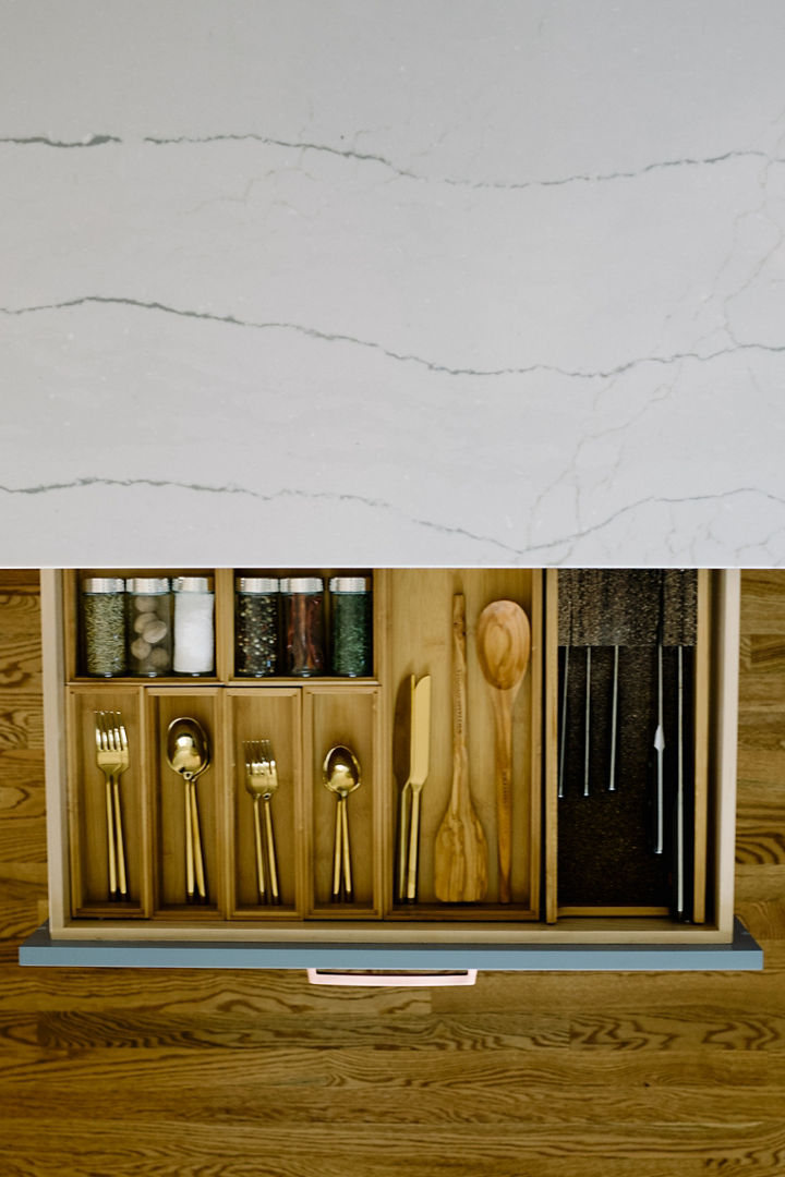 A kitchen island with a Cambria Ella quartz countertop with a pulled out drawer showing flatware, silverware, and spices.