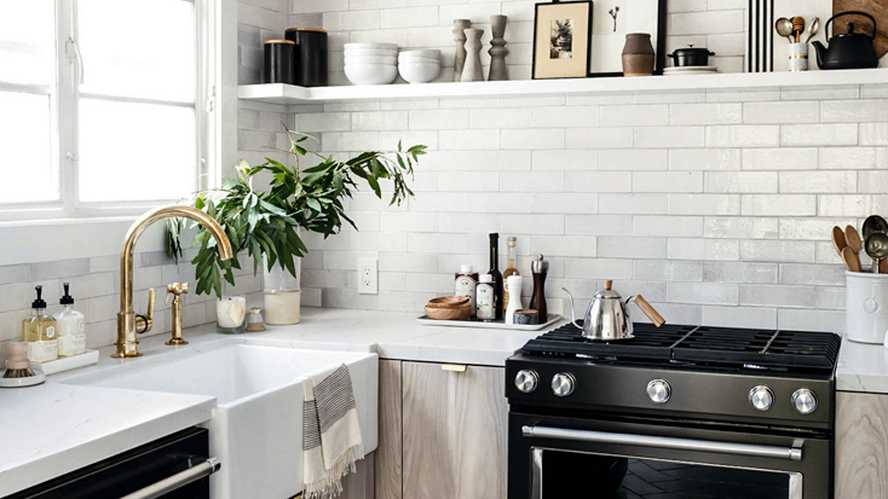 a neutral kitchen with herringbone tile floors, open shelving, glossy subway tile, light oak countertops, white quartz countertops, black appliances, and a farmhouse sink