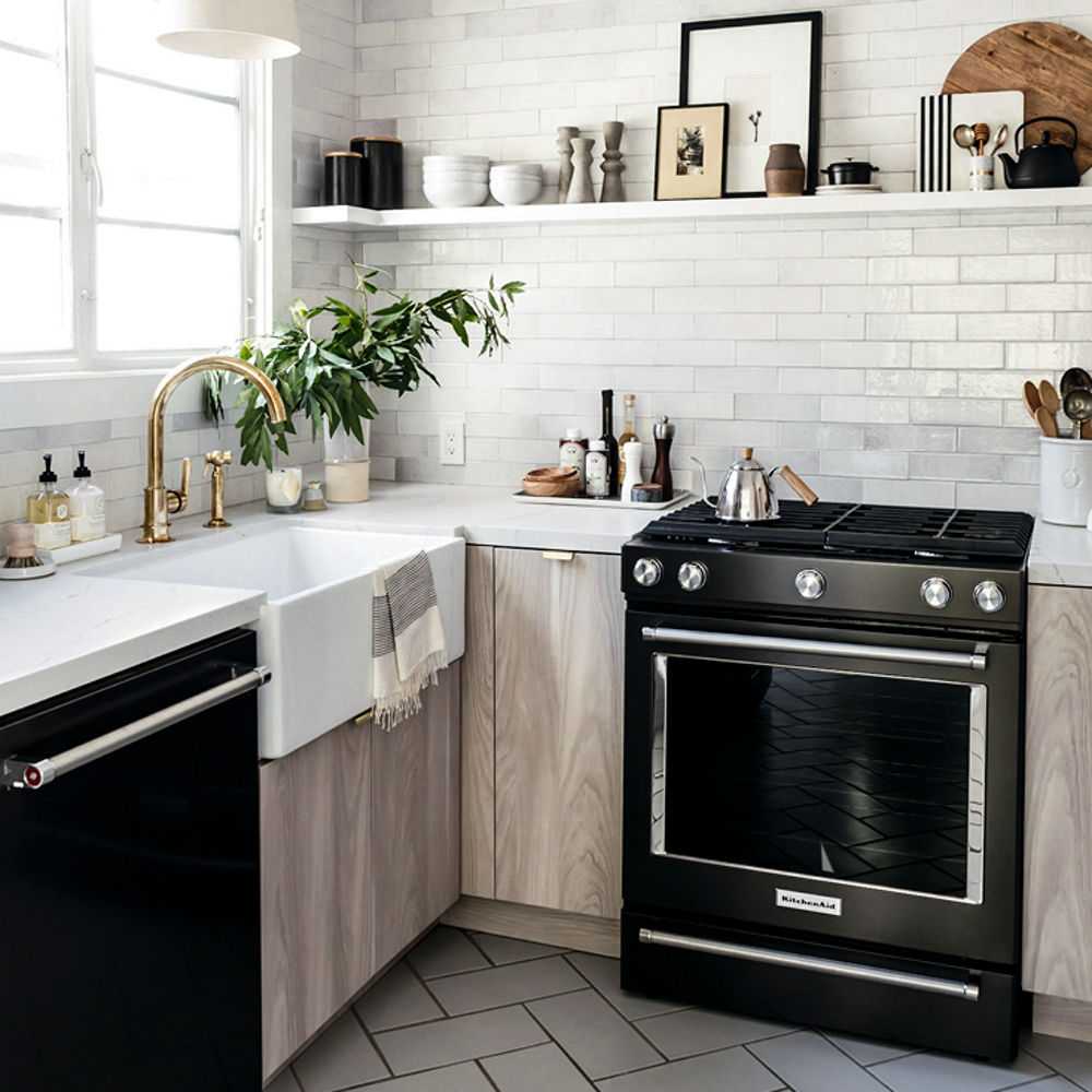 a neutral kitchen with herringbone tile floors, open shelving, glossy subway tile, light oak countertops, white quartz countertops, black appliances, and a farmhouse sink