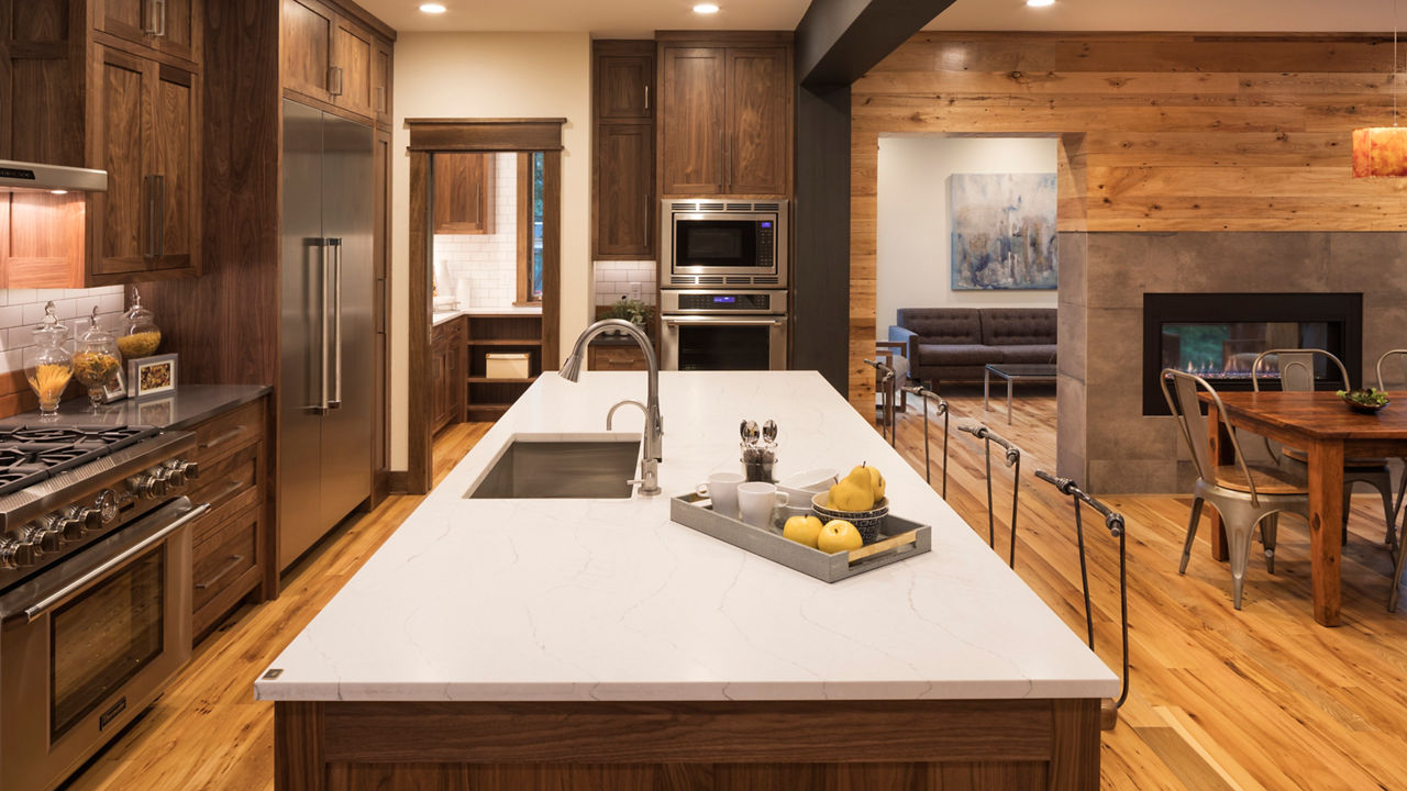 An open floor plan kitchen with natural light and dark walnut stained cabinets with Cambria Quartz Ella Matte countertops.