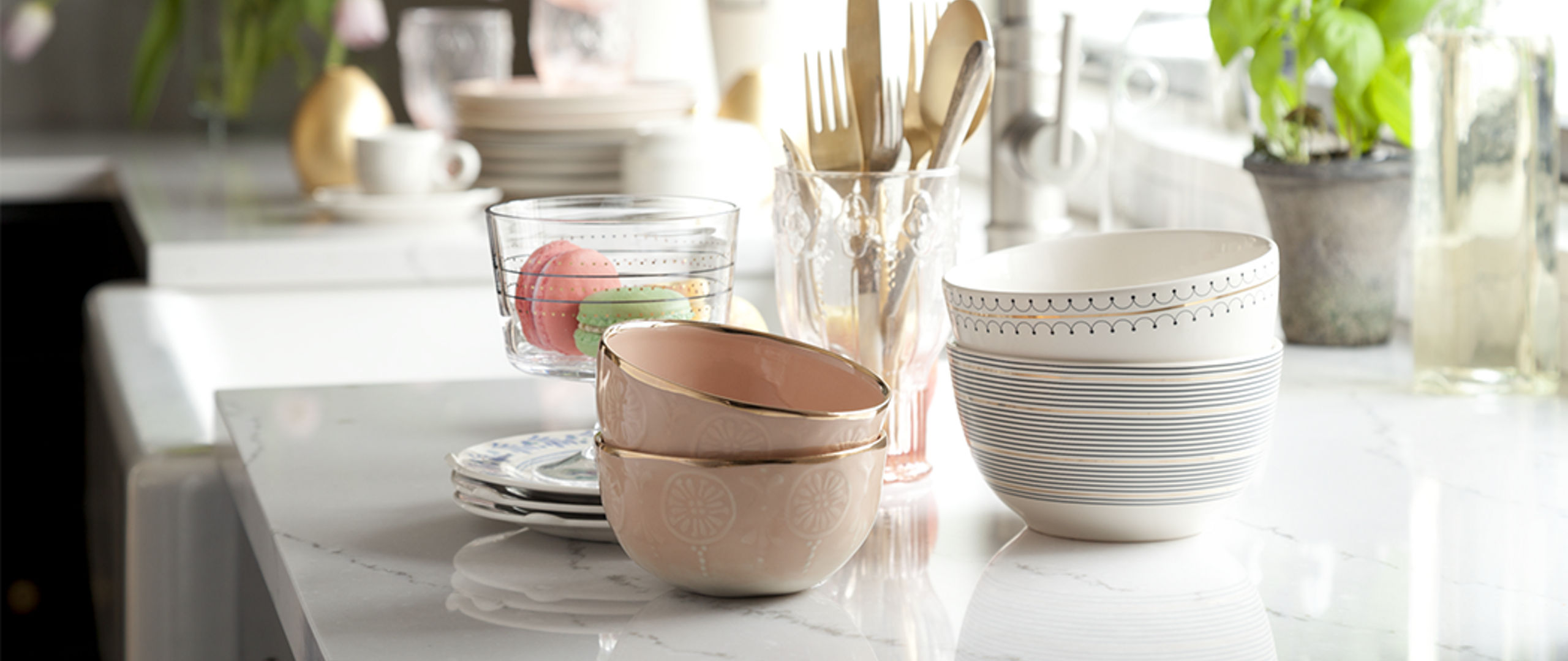 A kitchen with white quartz countertops and several stacked bowls and golden utensils on display.