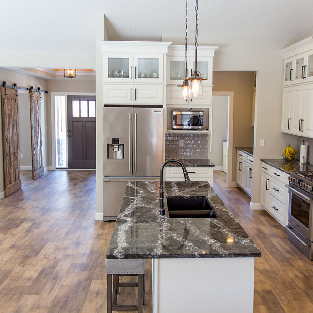 A open kitchen with white cabinets, light fixtures, and Ellesmere quartz countertops