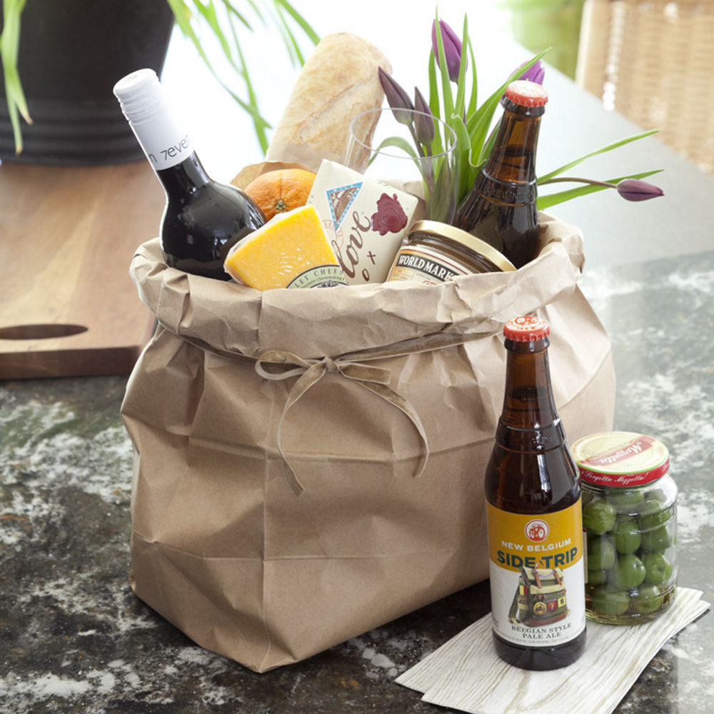 a hostest basket filled with wine, bread, flowers, and cheese.