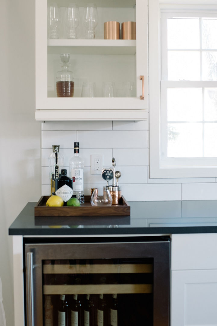 A beverage fridge is installed in a counter's side with a bar tray, and glass barware cabinet atop a Cambria Fieldstone quartz countertop.