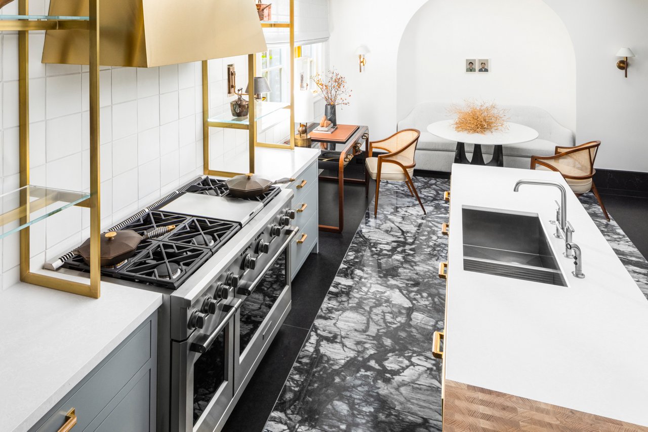 A bold kitchen with black and white marbled floors, gray kitchen cabinets and oak island cabinets, topped with Foggy City quartz countertops, with gold accents and a stunning gold hood over the range.