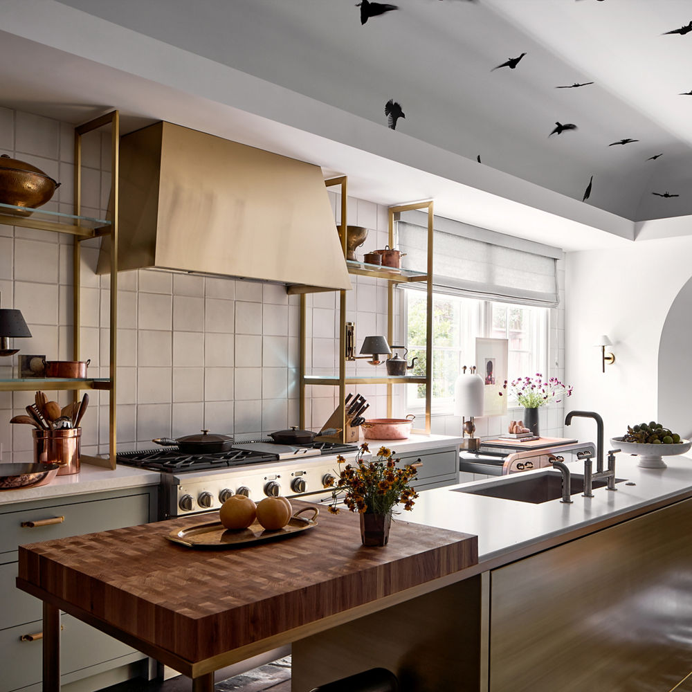 a kitchen with vaulted ceilings incorporating bird wallpaper, green lower cabinets, white quartz countertops, and gold accents throughout.