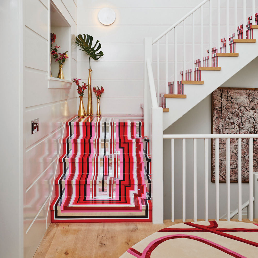A staircase with red, white, black, beige, and pink stripes along each step against a white wall and railing.