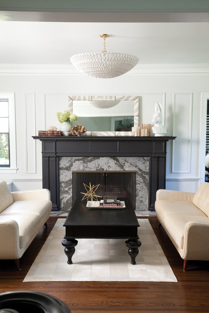 A modern farmhouse living room with beautiful quartz fireplace surround with a black mantel,  two white couches with a black coffee table in between, and white walls.
