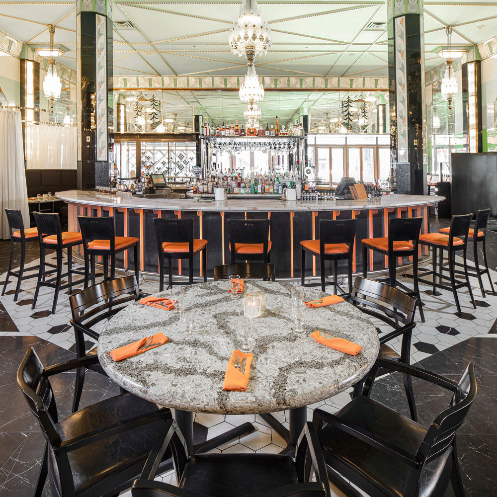 a restaurant and bar with tables and bartop topped with gray and white veined quartz countertops and orange seating and decorations