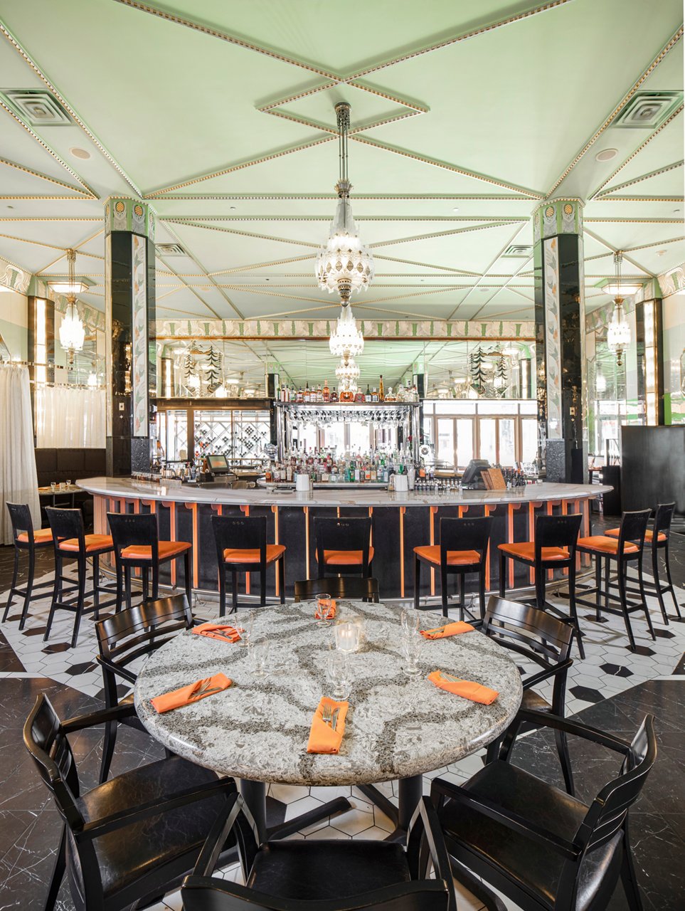 a restaurant and bar with tables and bartop topped with gray and white veined quartz countertops and orange seating and decorations