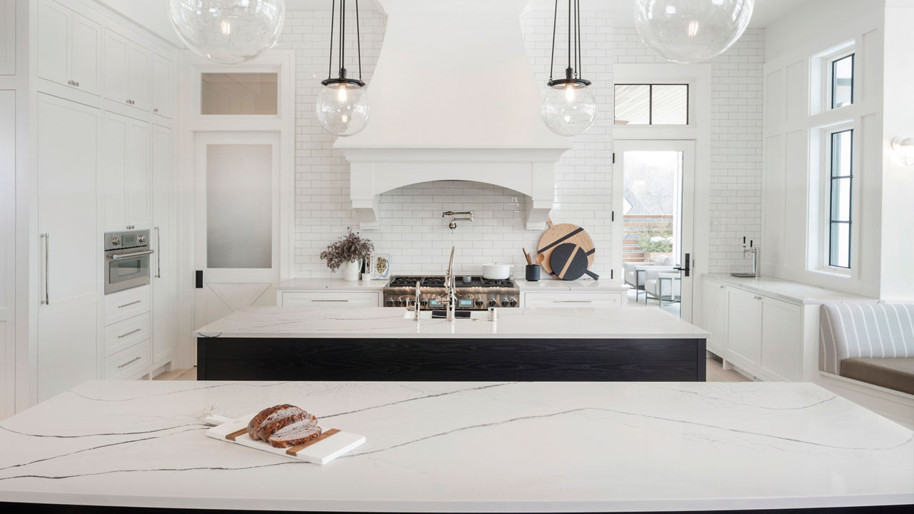 a traditional kitchen with white cabinets, a traditional white hood over a black and gold range, two black islands topped with white quartz countertops, and pendant lighting above each one.