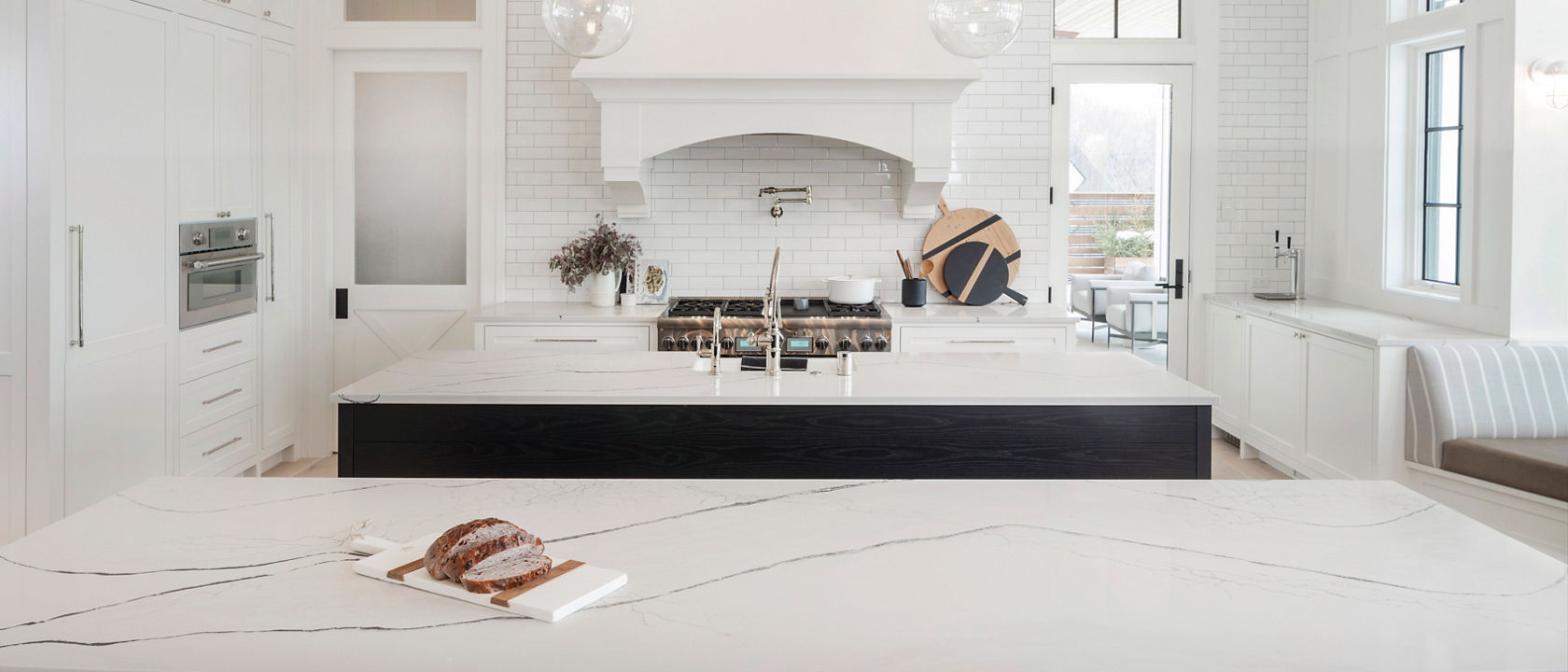 a traditional kitchen with white cabinets, a traditional white hood over a black and gold range, two black islands topped with white quartz countertops, and pendant lighting above each one.