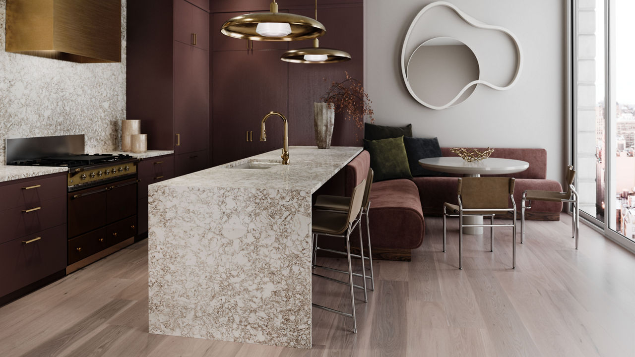 A gorgeous kitchen with dark mahogany cabinets, Cambria Hermitage™ quartz countertops, a gold hood over the range, gold pendant lighting, and a double waterfall kitchen island made from quartz. 