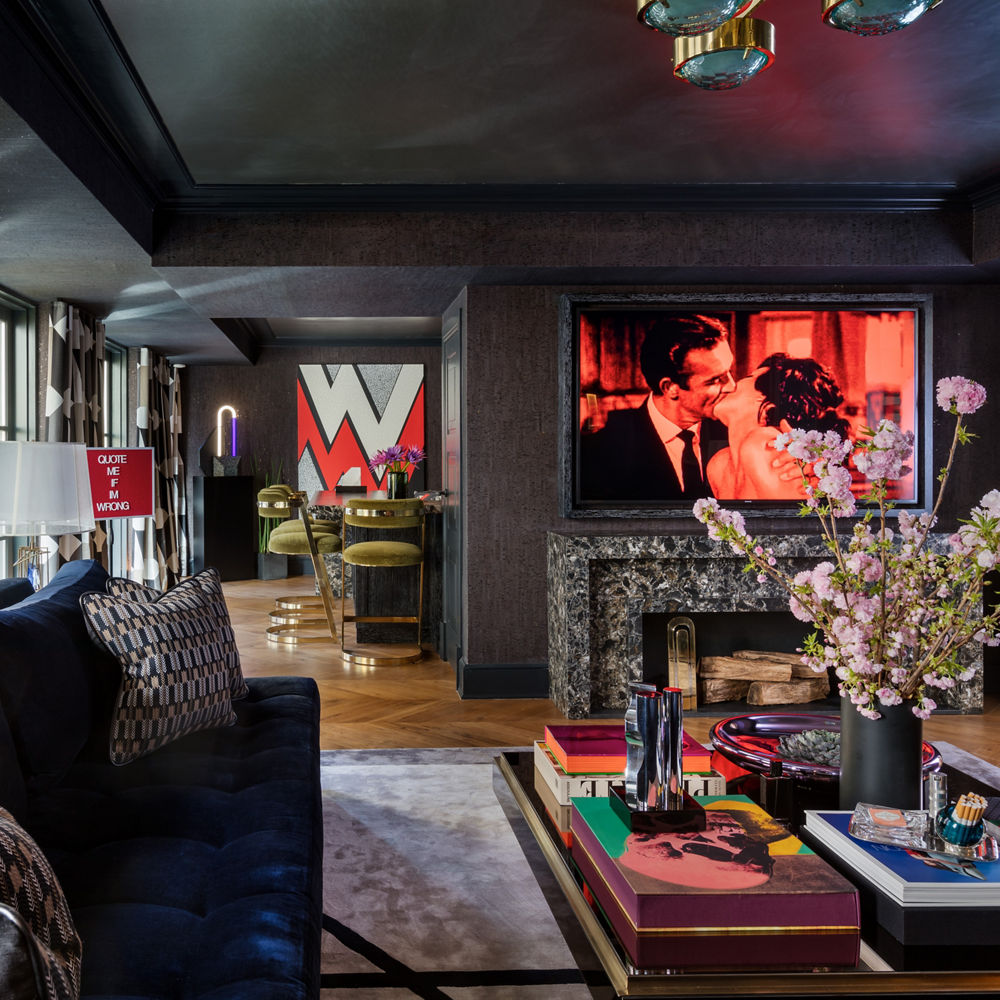 a bold living room with dark ceilings and walls, bold patterned curtains, a blue couch, and a black, white and gray speckled quartz fireplace.