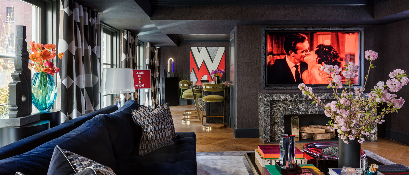 a bold living room with dark ceilings and walls, bold patterned curtains, a blue couch, and a black, white and gray speckled quartz fireplace.