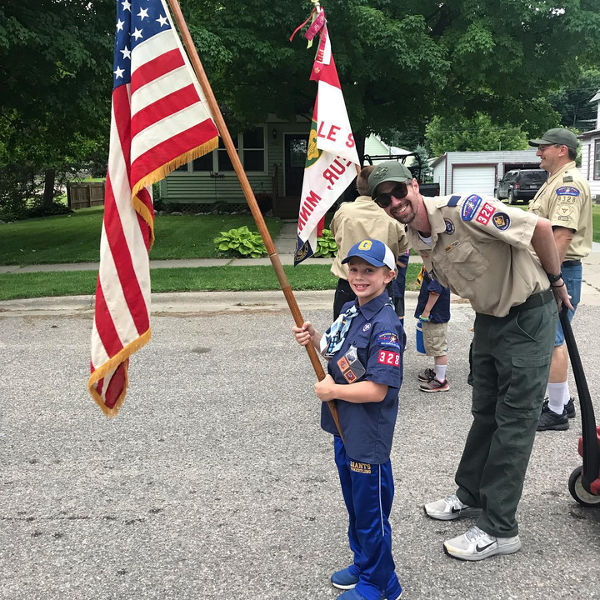 Eagle Scout stands next to Cub Scout son who is holding an American Flag