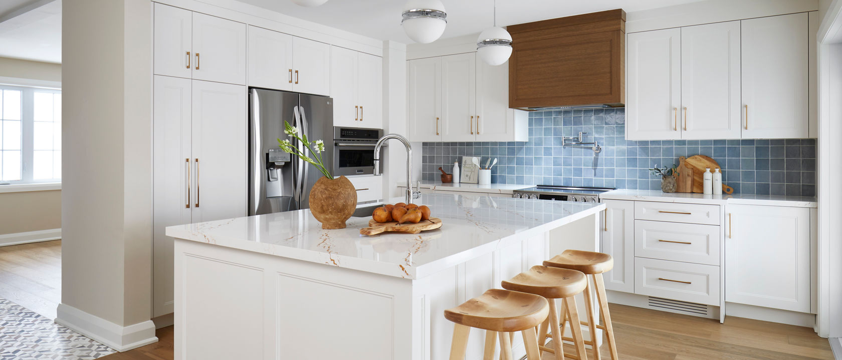 A bright white kitchen with a blue tile backsplash and white cabinets with Inverness Gold quartz countertops