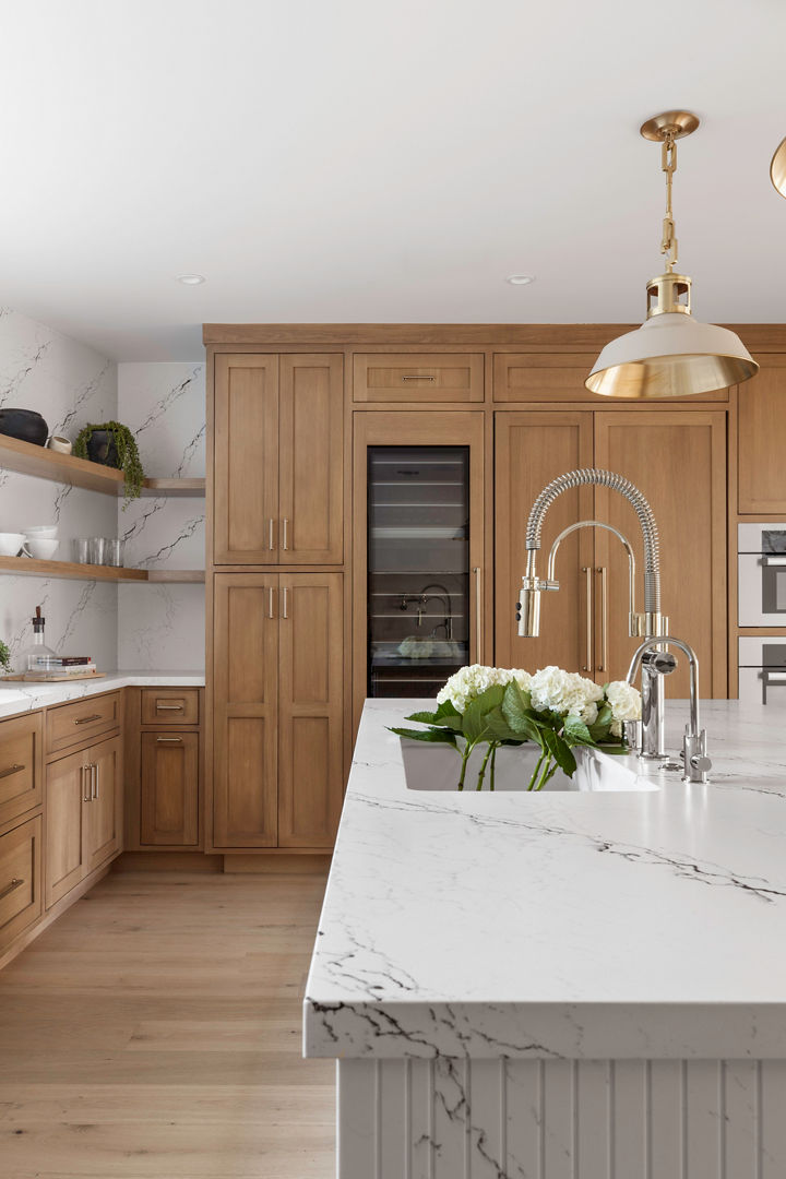 A stunning kitchen with light stained wooden cabinets, a double-waterfall edged island made from white quartz, matching quartz backsplash throughout the kitchen, and modern appliances.