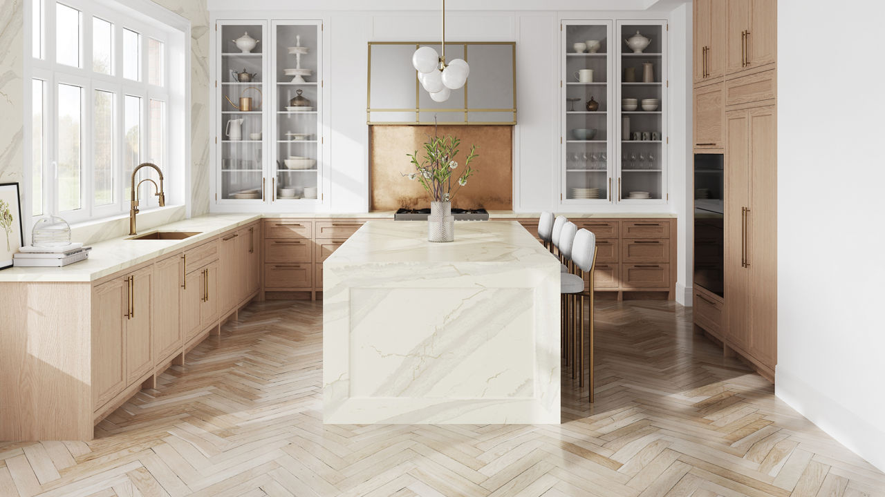 A warm white kitchen with a double waterfall kitchen island made from white quartz, light oak cabinets, herringbone wooden floor, and lots of natural light.