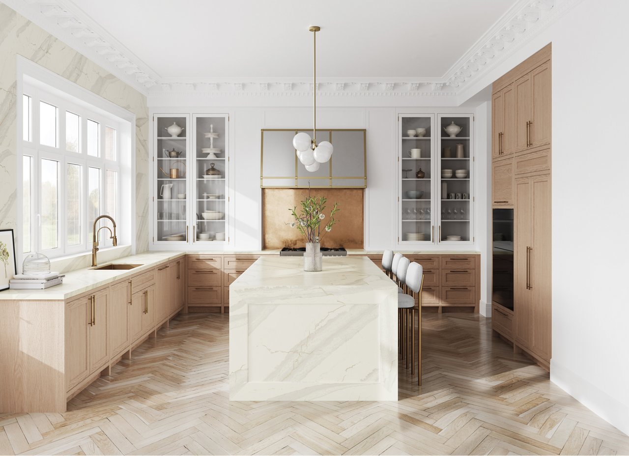 A warm white kitchen with a double waterfall kitchen island made from white quartz, light oak cabinets, herringbone wooden floor, and lots of natural light.