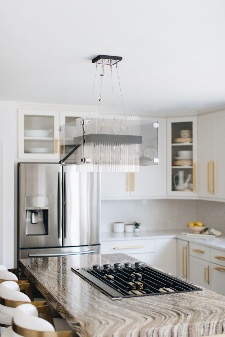 a kitchen with white cabinets, stainless steel appliances, gold handles, and a beige and brown quartz island