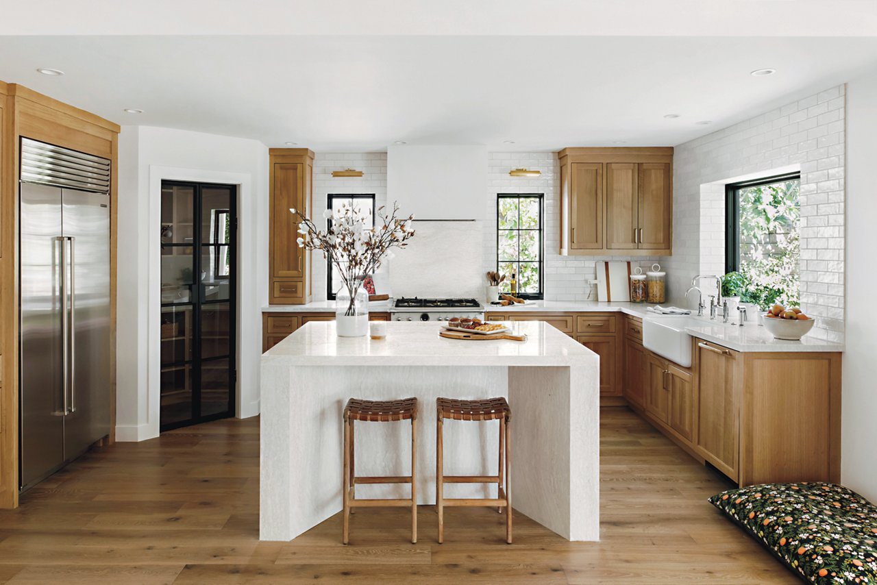 a farmhouse kitchen with oak cabinets, white quartz countertops, a center double waterfall island and a gorgeous pantry with a black door made from glass.