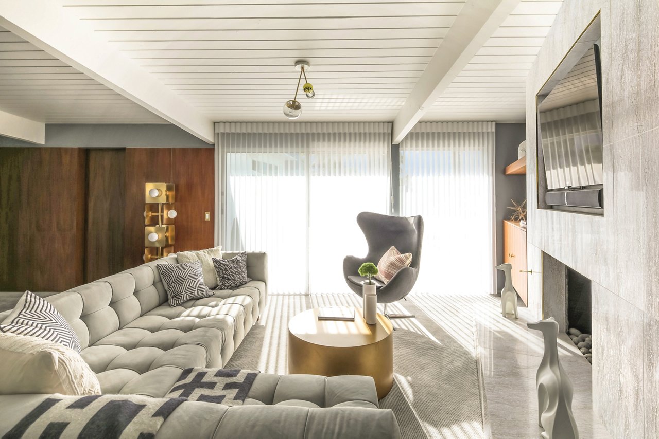 A mid-century modern sitting room with a white quartz fireplace, white couch and gray arm chair.