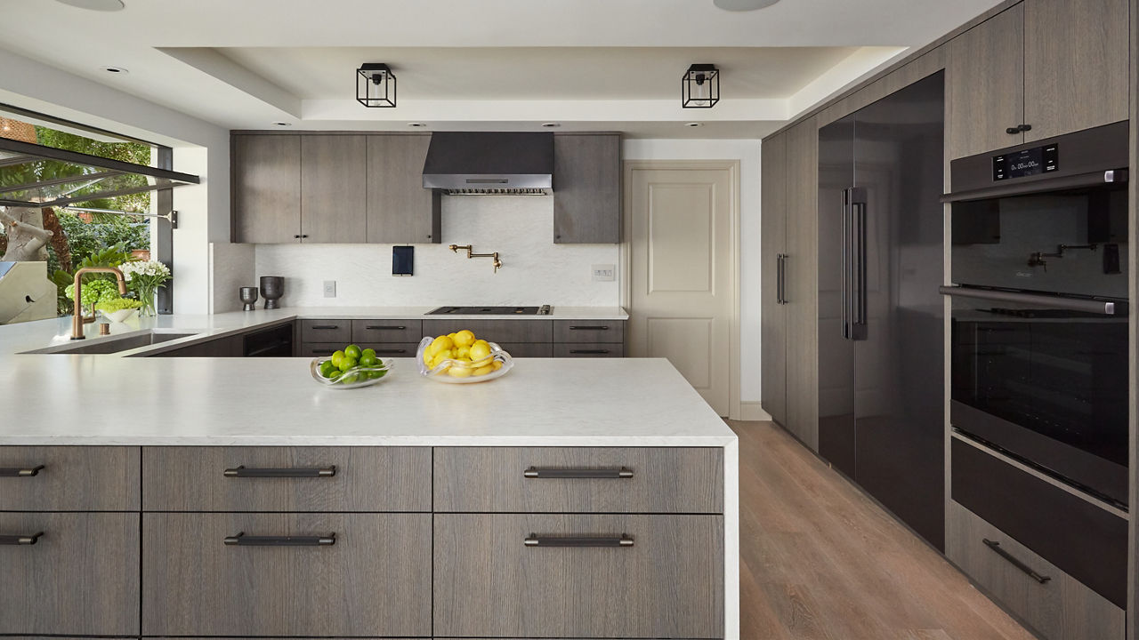 a neutral kitchen with gray-brown cabinets, matte black hardware, Cambria white quartz countertops and matching backsplash, and hard wood floors.