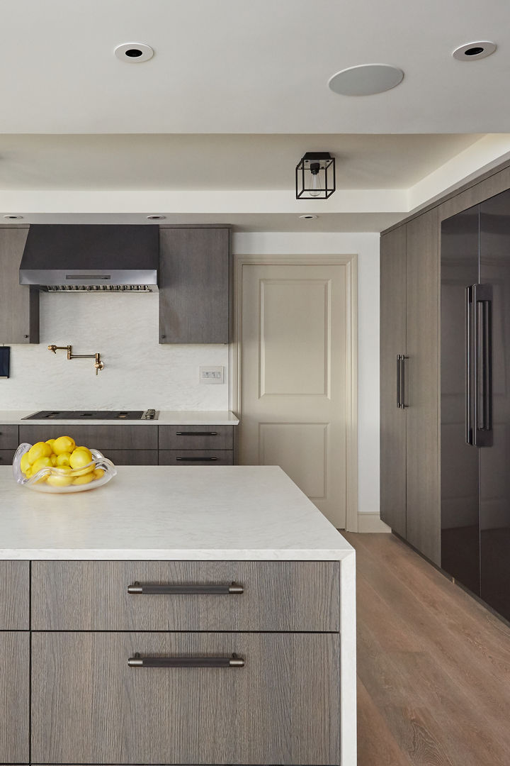 a neutral kitchen with gray-brown cabinets, matte black hardware, Cambria white quartz countertops and matching backsplash, and hard wood floors.