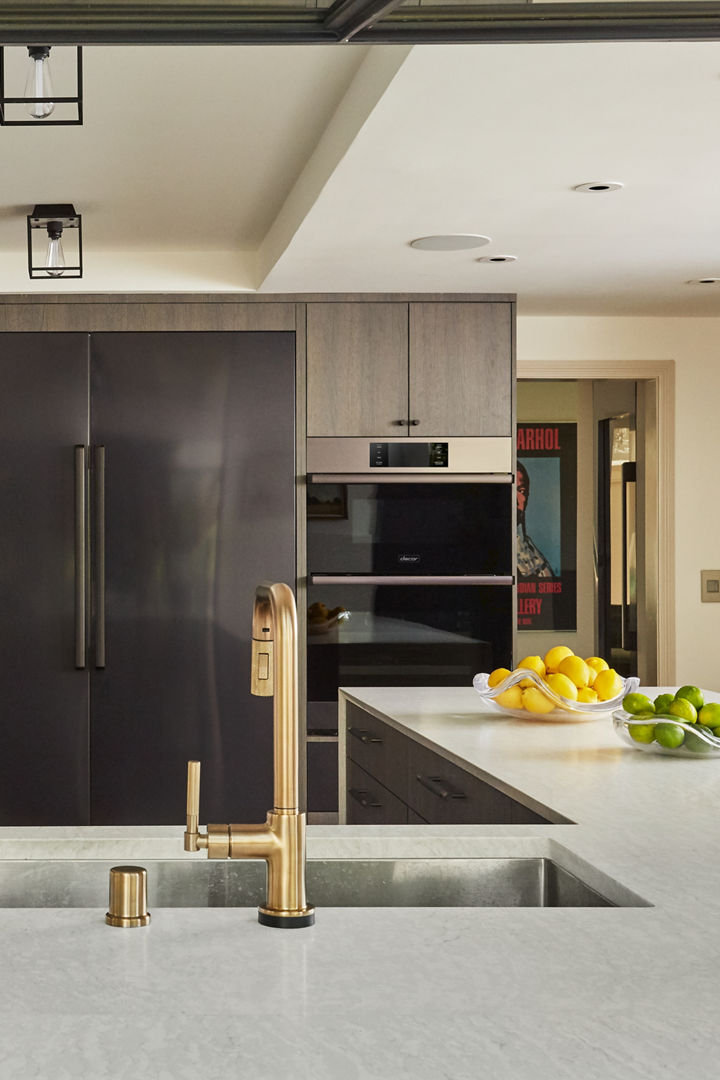 a neutral kitchen with gray-brown cabinets, matte black hardware, Cambria white quartz countertops and matching backsplash, and a sink with a golden faucet.