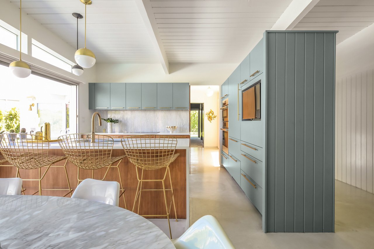 A mid-century modern kitchen with sage green upper cabinets, oak lower cabinets and island topped with white quartz countertops and white quartz backsplash.