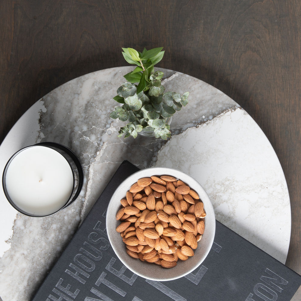 A gray and white veined lazy susan with a candle, book, and nuts on top.
