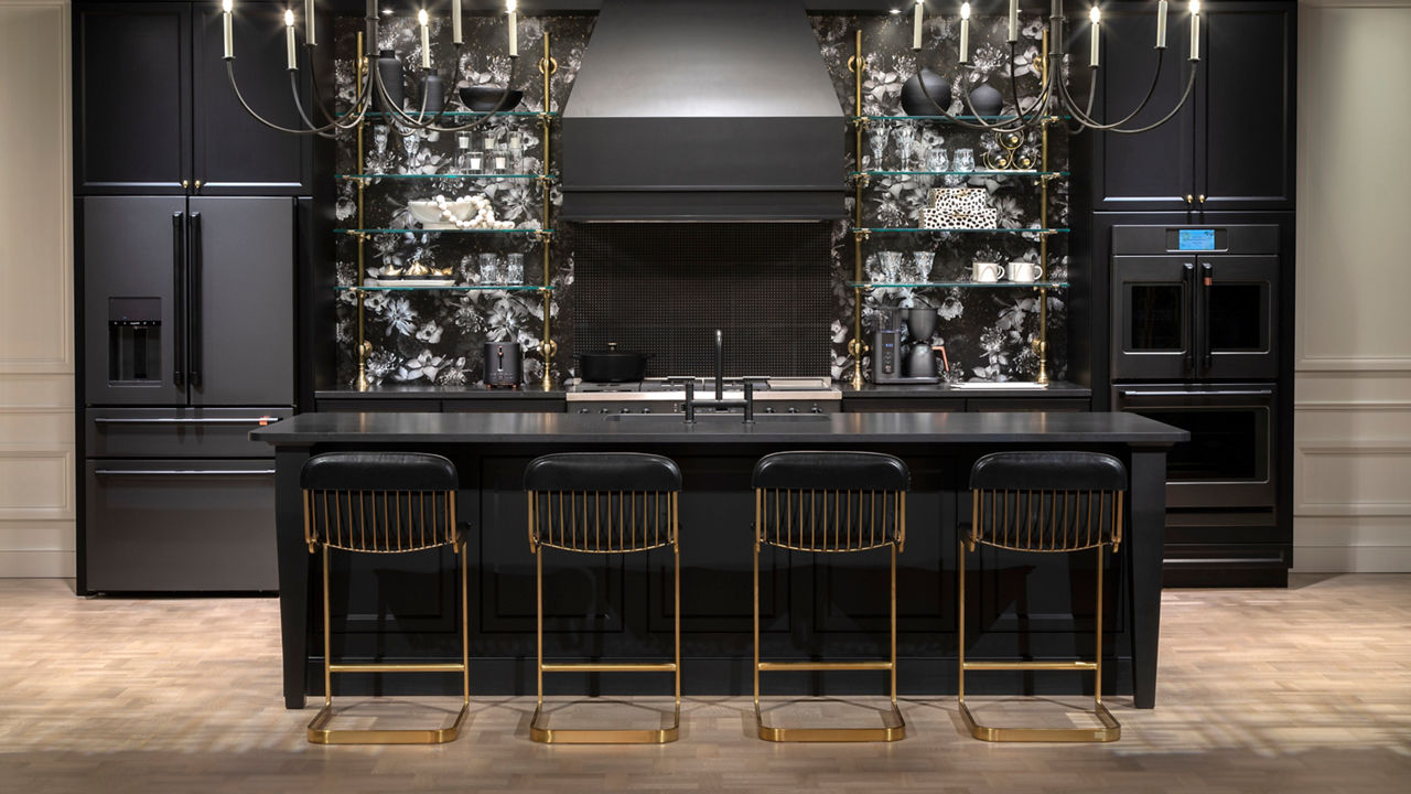 a luxurious black kitchen with black cabinets, black quartz countertops, black GE appliances, and a white and black floral wallpaper with a black tiled backsplash.