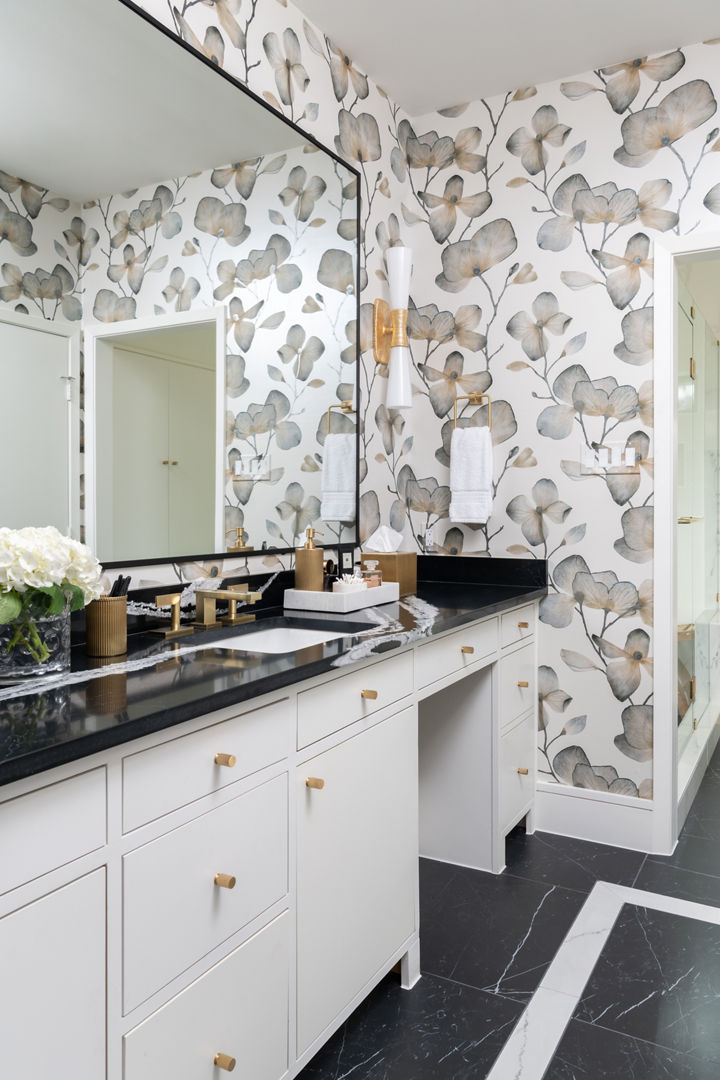 a unique bathroom with a white vanity topped with black and white veined quartz countertops, bold floral wallpaper, black tiled flooring, and a large mirror.