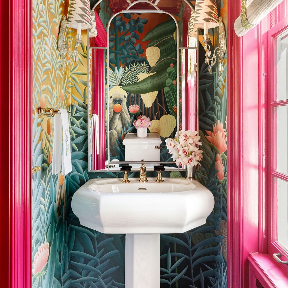 a bold powder bathroom with hot pink trim on the door and window, black and white quartz tiled floor, rainforest inspired wallpaper and a pedestal sink.