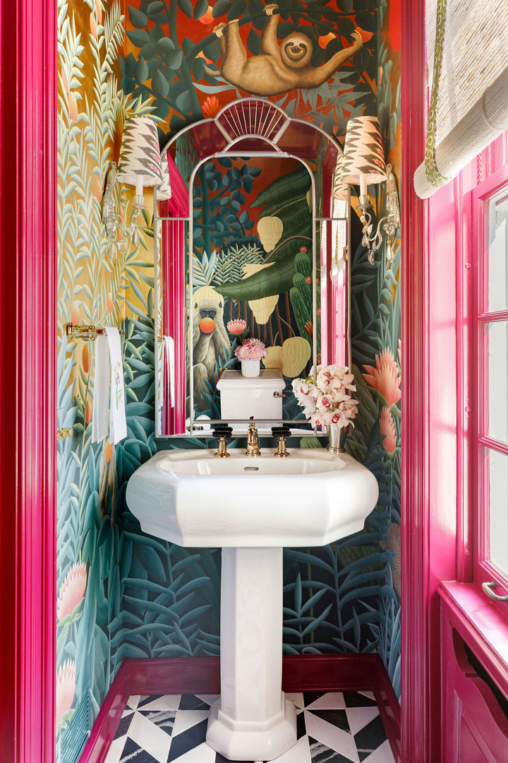 a bold powder bathroom with hot pink trim on the door and window, black and white quartz tiled floor, rainforest inspired wallpaper and a pedestal sink.