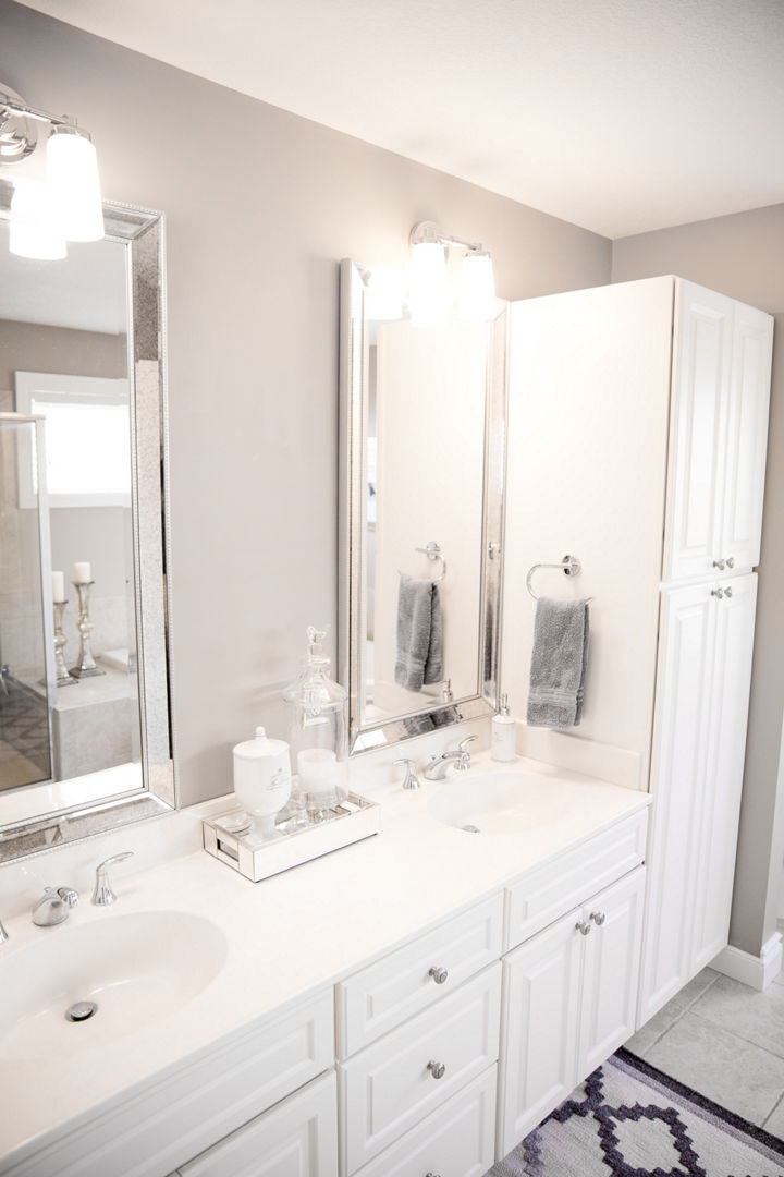 A bathroom with two mirrors and white drawers and cabinets.