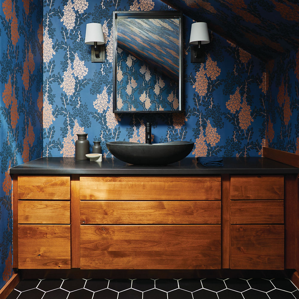 A bathroom with bold blue wallpaper, a wooden vanity, and black white quartz countertops.